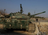 Men walk near an abandoned tank that belongs to the ousted Syrian President Bashar al-Assad's forces, on the outskirts of Damascus