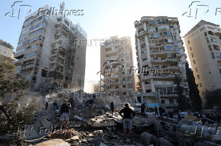 People stand on rubble at a damaged site in the aftermath of an Israeli strike in Tayouneh