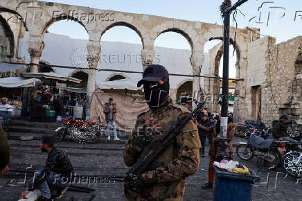 A fighter of the ruling Syrian body flashes a victory sign as he stands outside the Umayyad Mosque, in Damascus