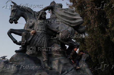 Boys play on the Salah Al Din Statue, in Damascus