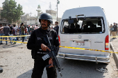 Police officer stands guard near a cordoned damaged vehicle at the site after a suicide blast in Karachi