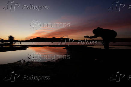 A man takes photos of sand dunes and palm trees partially covered by floodwaters, after rare rainfall hit the area last September, at dawn in Merzouga