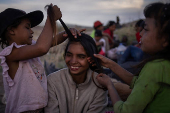 Girls brush the hair of a fellow migrant along international boundary of U.S. and Mexico