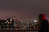 A woman takes a picture on her mobile phone of the Canary Wharf skyline from the Royal Docks during foggy weather in London