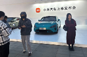 People pose for pictures in front of Xiaomi's first electric vehicle SU7 that is displayed outside the avenue for the car's launch event in Beijing