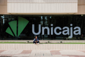 A woman sits next to the new logo of Unicaja outside of a Unicaja bank branch office in Malaga