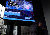 A man stands next to an electronic board showing Nikkei share average in Tokyo