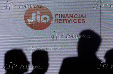 FILE PHOTO: People stand next to a logo of Jio Financial Services ahead of its listing ceremony at the Bombay Stock Exchange in Mumbai