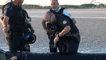 A police officer uses a knife to slash a dinghy after it was abandoned by migrants trying to cross the English Channel on a beach at Gravelines