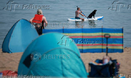 A man sits on a paddleboard with his dog near the beach at Rhos-on-Sea, Wales