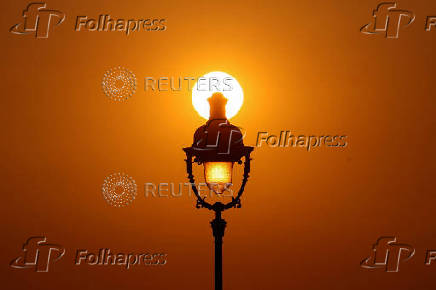 The sun sets behind a street lamp