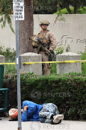 A U.S. Marine guards a federal building as a homeless man sleeps in the sidewalk, in Los Angeles