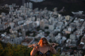 A woman fixes her hair to take a photo during sunrise at Dona Marta lookout point in Rio de Janeiro