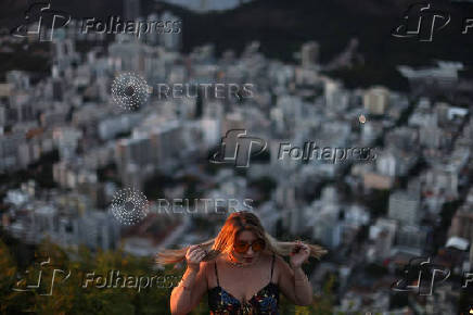 A woman fixes her hair to take a photo during sunrise at Dona Marta lookout point in Rio de Janeiro