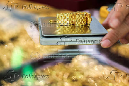 A gold seller weighs a gold watch bracelet inside a gold shop, on the day that gold surges to set a fresh record high, in Bangkok
