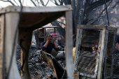 A man sits near the remains of his burned house after a fire at a slum area in Rohini