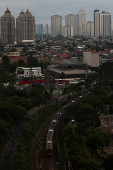 A commuter train rides as high rises buildings stand in the background in Jakarta
