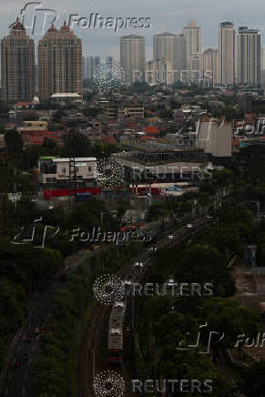 A commuter train rides as high rises buildings stand in the background in Jakarta