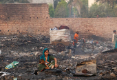 A woman sits with a child on her lap next to the remains of her burned house after a fire at a slum area in Rohini