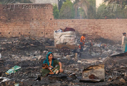 A woman sits with a child on her lap next to the remains of her burned house after a fire at a slum area in Rohini
