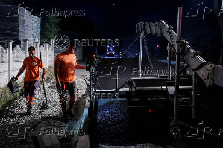 Workers lay asphalt at night to avoid the daytime heat wave, in Rahovec
