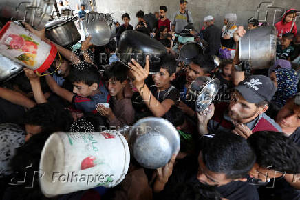 Palestinians wait to receive food cooked by a charity kitchen, in Gaza City