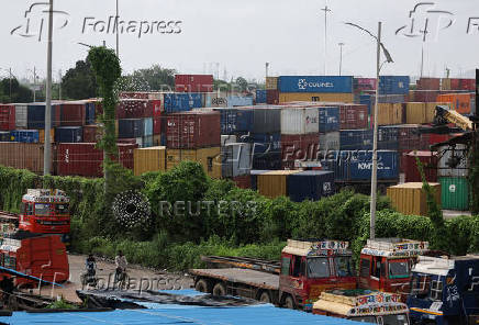 Men ride bicycles past shipping containers at a warehouse in Navi Mumbai