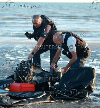 Police officers examine the motor on a dinghy after it was abandoned by migrants trying to cross the English Channel on a beach at Gravelines
