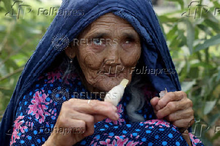 Haleema Bibi, 80, eats an ice-cream on a roadside as she waits to leave, after Pakistan started to deport documented Afghan refugees, outside the United Nations High Commissioner for Refugees (UNHCR) repatriation centre in Nowshera