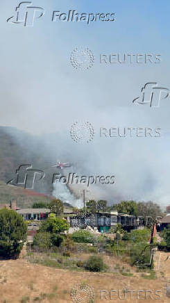 A firefighting helicopter works to extinguish the Rancho Fire as smoke rises at Laguna Beach
