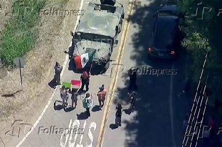 Protesters holding a Mexican flag try to block a military convoy during an immigration raid on an agricultural facility in Camarillo