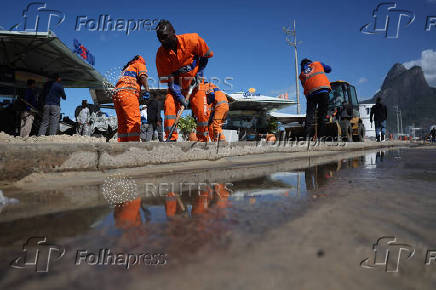 Workers clear sand on the shore of Leblon beach after big waves hit Rio de Janeiro