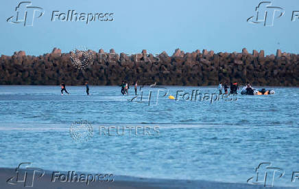 A group of migrants carrying life jackets and rubber rings walk through the water after abandoning a dinghy whilst trying to cross the English Channel on a beach at Gravelines