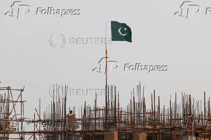 A Pakistani flag flutters over iron scaffoldings as a labourer works at a construction site on the eve of Pakistan's Independence Day celebrations, in Lahore