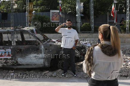 A man poses for a photo next to an ambulance burned by Israeli attacks, on a street in Tehran