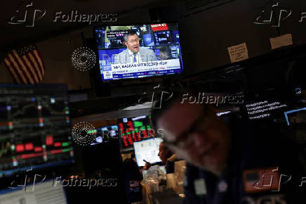 A screen displays news on S&P 500 and NASDAQ stock market indices as traders work on the floor at the New York Stock Exchange (NYSE) in New York City