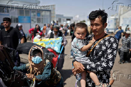 An Afghan who was deported from Iran, holds his child as he arrives at a camp for returning migrants near Islam Qala border crossing