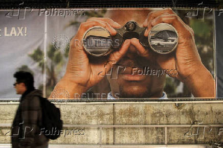 FILE PHOTO: A man walks past a billboard at an airport construction area after a shooting at the Los Angeles International Airport