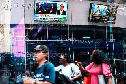 A person walks near a screen showing U.S. President Donald Trump meeting with Russian President Vladimir Putin in Alaska, at the Nasdaq Market site in New York