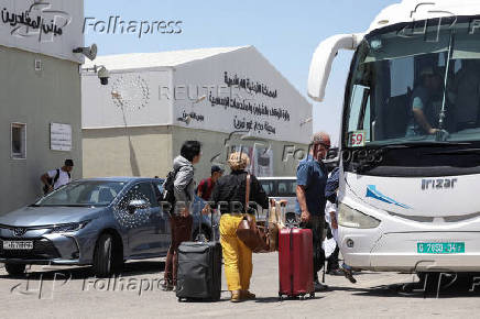 Expats, including diplomats from different nationalities, who were stranded in West Bank and Israel, board a bus as they hold belongings while being evacuated through the King Hussein Bridge crossing, in South Shuna