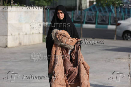 A woman holds the clothes of one of the victims of the Israeli attacks, in a street in Tehran