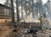 A firefighter stands near smoldering debris amid the charred remains of a burned structure near the Grand Canyon Lodge