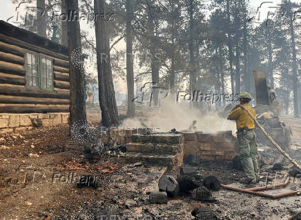 A firefighter stands near smoldering debris amid the charred remains of a burned structure near the Grand Canyon Lodge