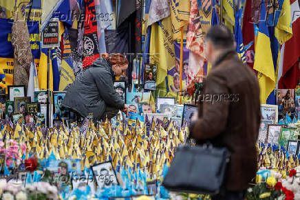 Woman places a flag at the makeshift memorial to fallen Ukrainian defenders at Independence Square in Kyiv