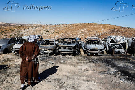 A Palestinian man inspects burnt cars, after Israeli settlers set fire to cars in the Palestinian town of Burqa