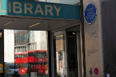 A double-decker bus is reflected in a window next to the John Harvard blue plaque outside the John Harvard Library on Borough High Street, London