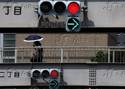 A woman holding a parasol walks on a pedestrian bridge near traffic signals, in Tokyo