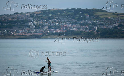 A man stands on a paddleboard with his dog near the beach at Rhos-on-Sea, Wales