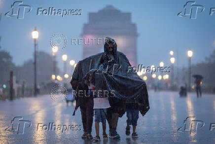 A family uses a plastic sheet to protect themselves during heavy rains in New Delhi
