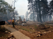A firefighter stands near smoldering debris and active flames amid the charred remains of a burned structure near the Grand Canyon Lodge